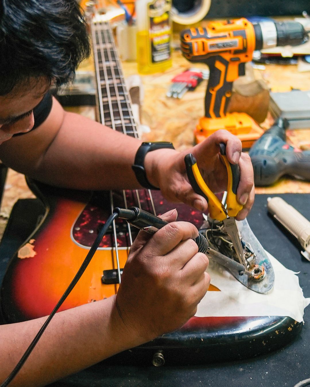 Guitar technician working on a guitar with tools on a wooden workbench